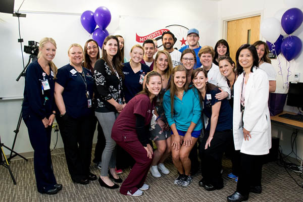 Schroder, a young man who coped with testicular cancer, poses with former Colorado Rockies player, Vinny Castillo, at the UCHealth University of Colorado Cancer Center. This is a big group photo with balloons.