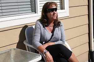 A blind woman sits outside her home. She now has a bionic eye and uses it to find her way around her home.