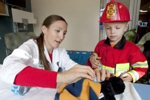 ER doctor puts a cast on a stuffed animal while boy in a fire costume watches.