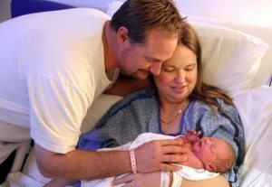 Mom holds her newborn while dad leans in to touch the newborn's face.