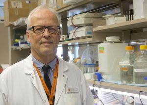 Dr. Eric Poeshcla, chief of Immunology at the University of Colorado School of Medicine, poses in his lab. He's wearing a white coat.
