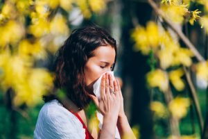 A woman with trees behind her covering her nose with a Kleenex