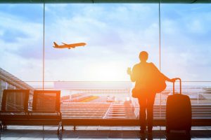 A photo of a woman looking out the window at an airport as a plane takes off.