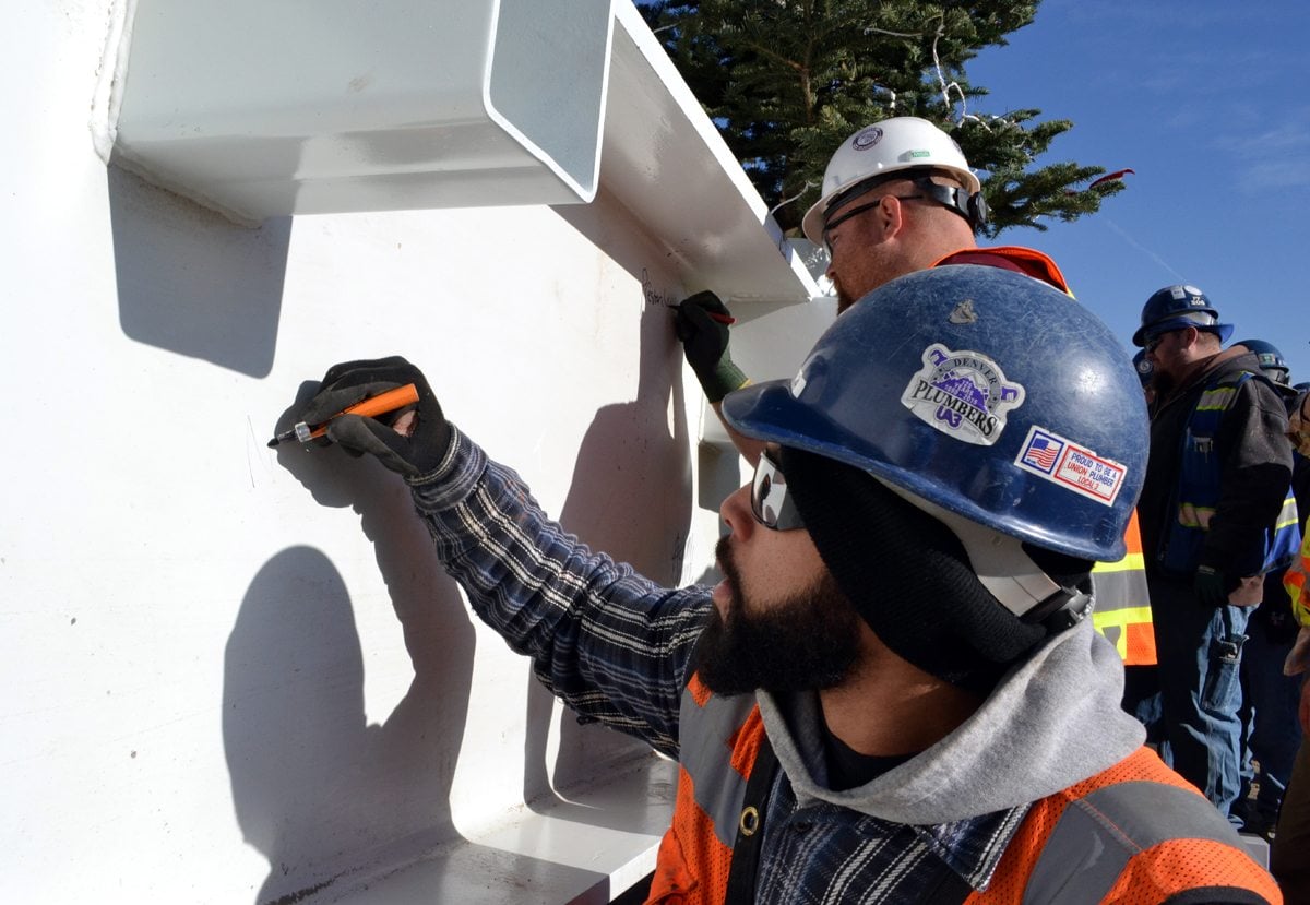 A plumber signs his name on a beam that was placed at one of the highest points of the UCHealth Greeley Hospital building, which is under construction.