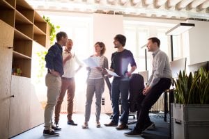 People in an office stand around like they're discussing a project together.