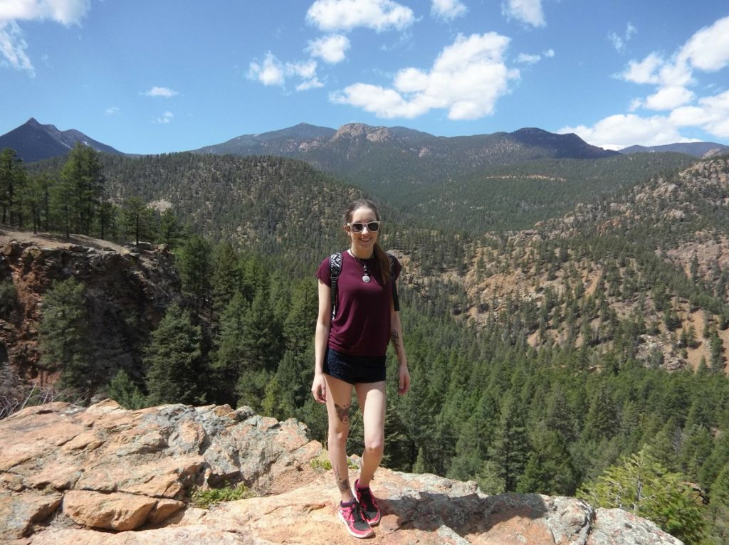 Hannah Moraski poses on a red rock with mountains beheind her. She loves hiking in Colorado.