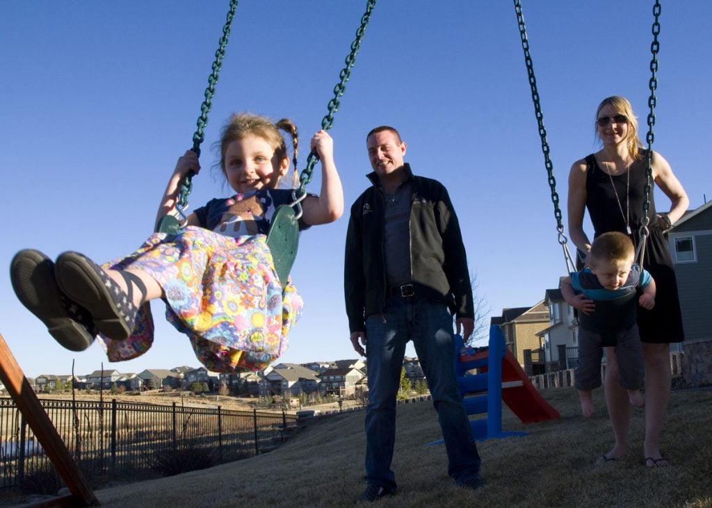 A mom and dad gently push their two children on swings.