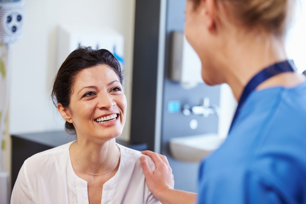 Female Patient Being Reassured By Doctor In Hospital Room for health screenings