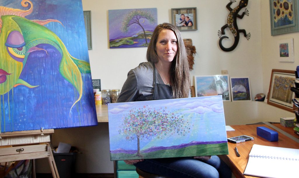 Artist Tanielle Childres sits in her Loveland studio. Childres said she aims to paint the beauty in sorrow, not just the sorrow, and the two paintingsthe one in her arms and the hanging on the wall behind her were created in memory of her two unborn children, and now prints of them hang in units at PVH and MCR.