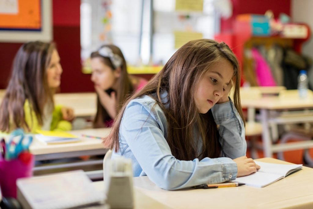 A teen girl at a student's desk. She looks depressed.
