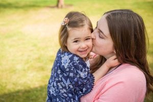 mom kisses daughter, who is a toddler, on the cheek.