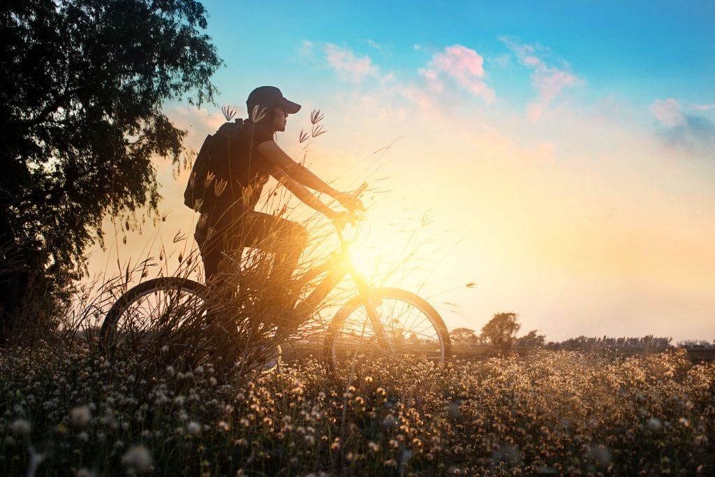 Biker on mountain bike adventure in beautiful flowers nature of summer sunset background
