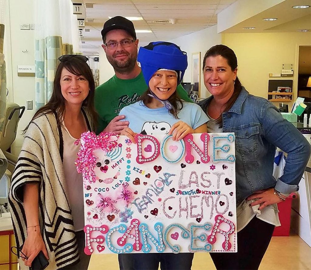 Louisa Drouet poses with supporters on the last day of chemo. She is wearing a big blue cap. It's called a cold cap and it helps women keep their hair. She's holding a sign that says "Last chemo"