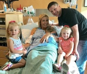 mom in the hospital holding new baby, with dad and two daughters at her side, right before mom experienced placenta accreta.