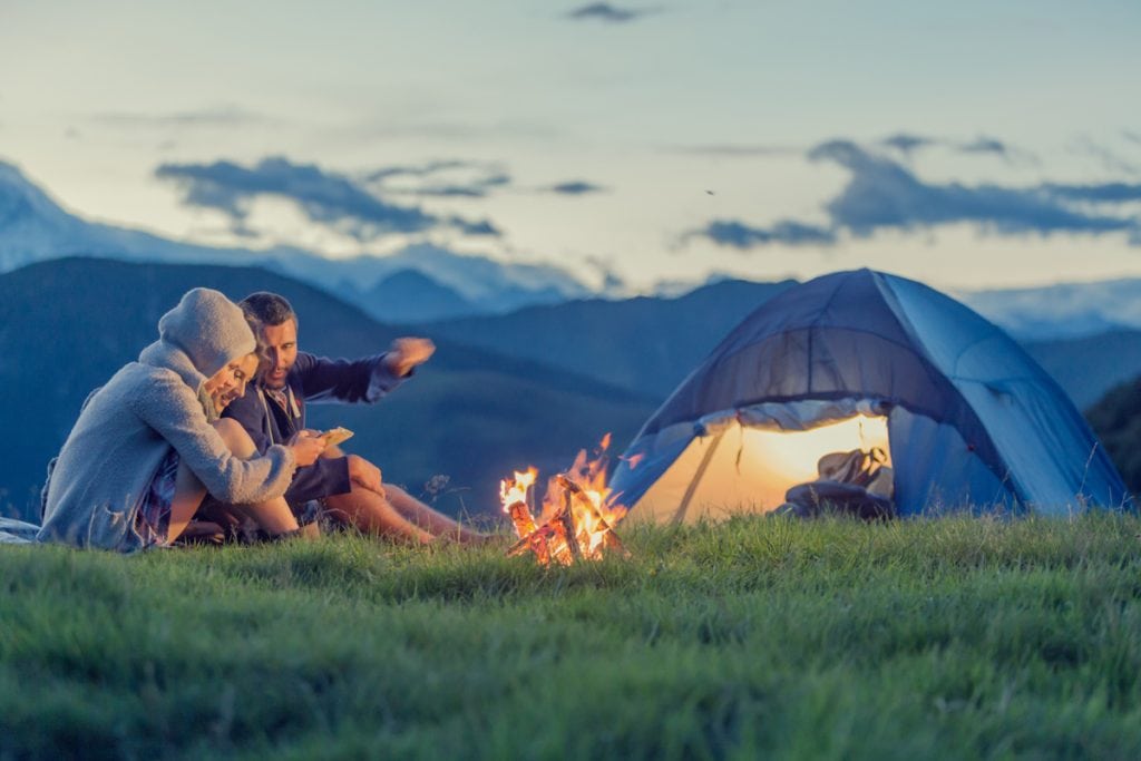 Three young people camping with tent in background