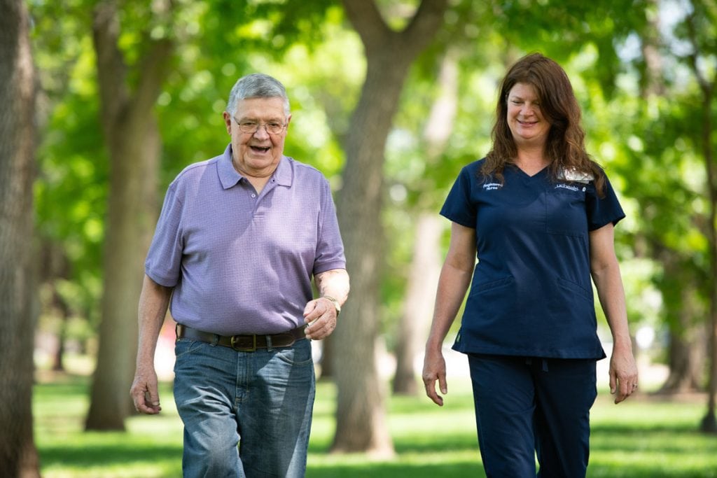 a man walks in a park with his nurse navigator outside UCHealth Memorial Hospital.