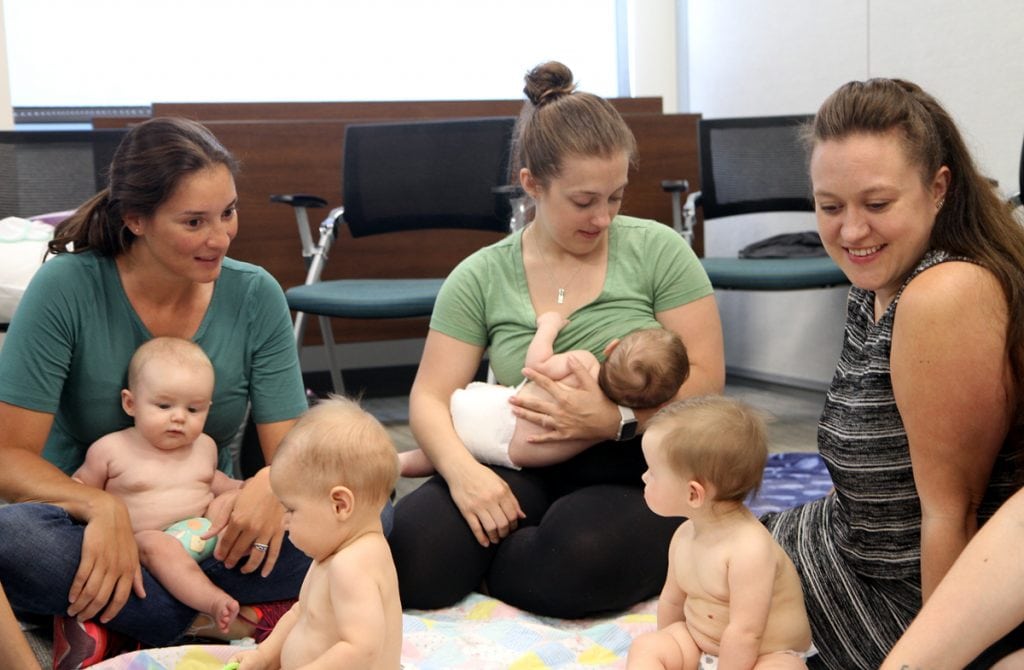 mothers and babies gather around a blanket to talk and play at a breastfeeding support group.