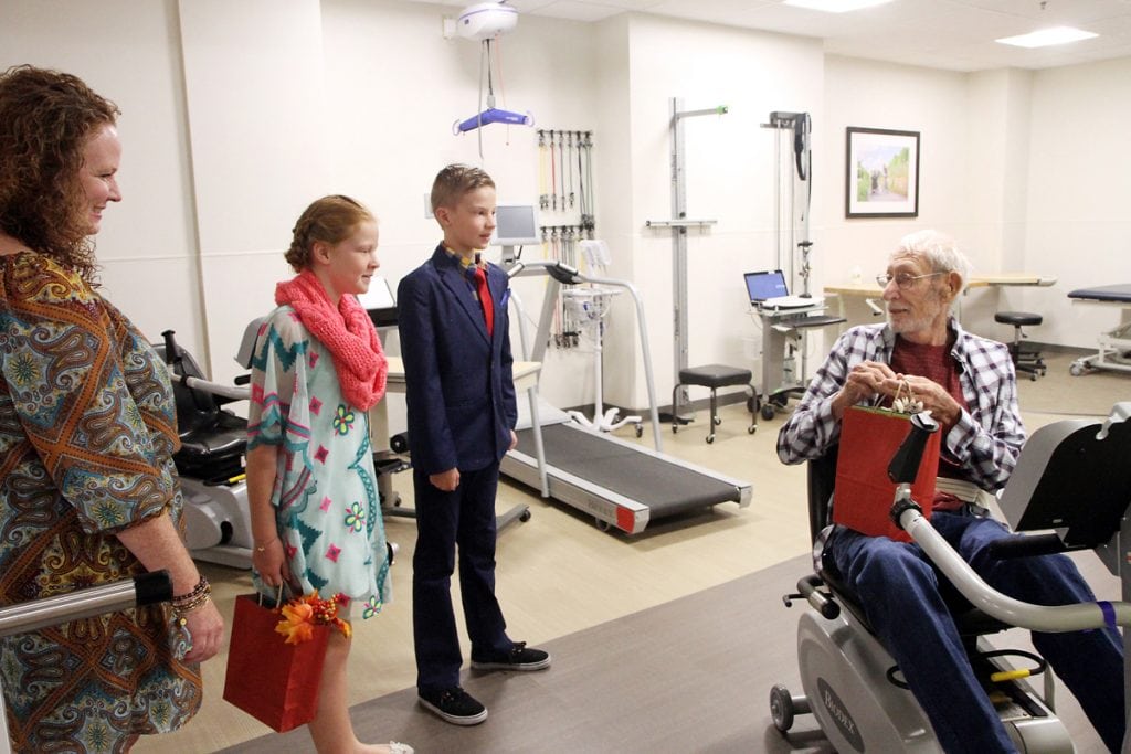Charlie and his family talk with a patient on a incumbent bike in the rehab gym.