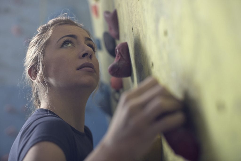 Young female climber hand gripping hold on rock climbing wall