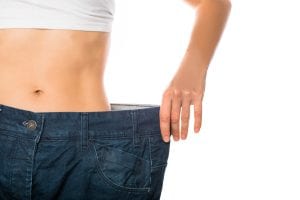 Slim stomach of young woman, thin body with perfect waist, showing her jeans after successful diet or sport training on isolated