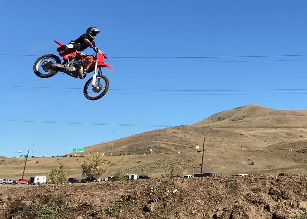 Eric Rice rides a motocross bike and flies over a dirt mound.