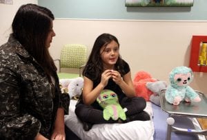 Marlie sits on a hospital bed talking while her mother listens next to her.