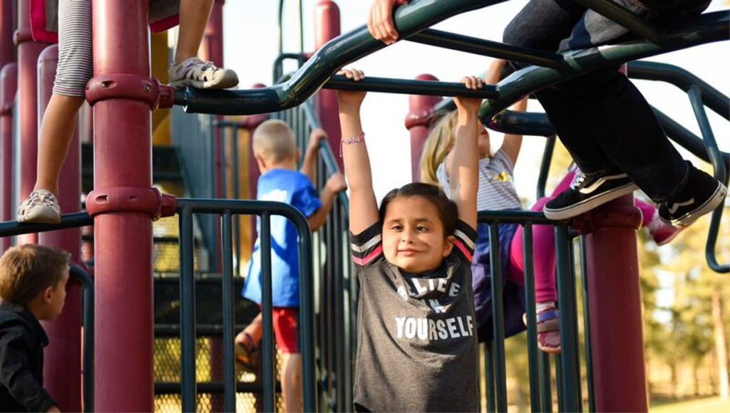 Grace Cuellar swinging from playground equipment.