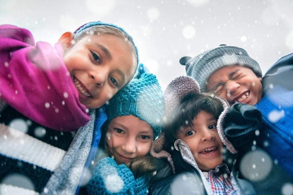 This photo shows children outside in warm coats and hats as snow begins to fall.