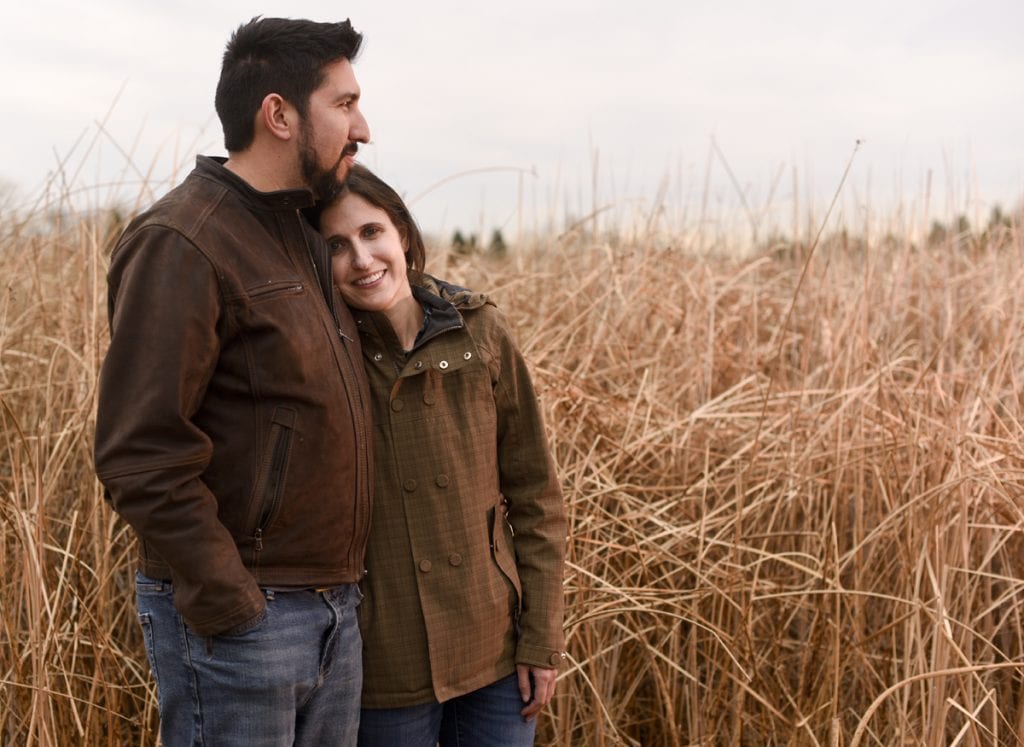 A woman and her husband pose for a picture near a wetland. He's hugging her. She survived a rare polio-like illness called AFM.