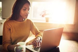 woman drinking coffee at her laptop in the morning, which is a great time to thing of ideas for social distancing for that day.