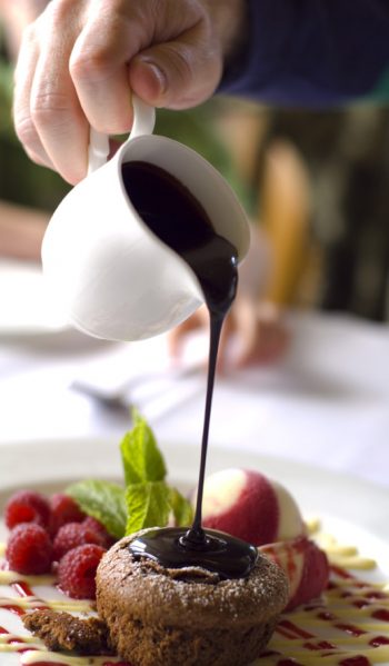Photo of chocolate sauce over a chocolate souflee with fruit.