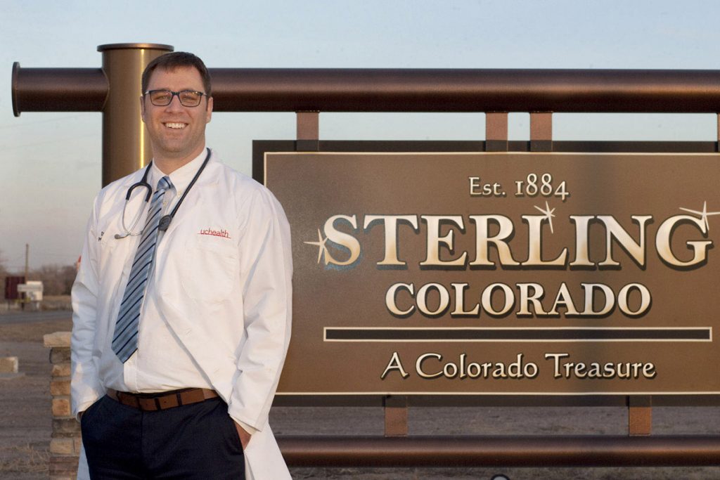 Dr. Daniel Lambrecht stands in front of a sign welcoming people to Sterling, Colorado