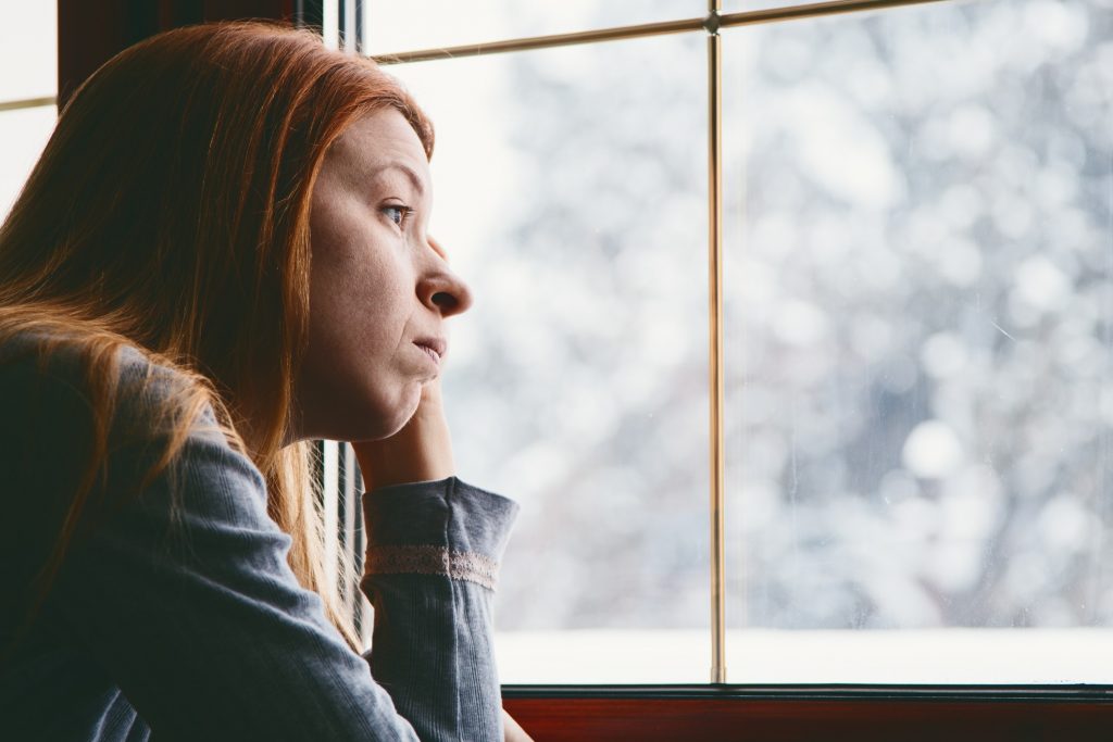 A sad woman looks out the window on a winter day.