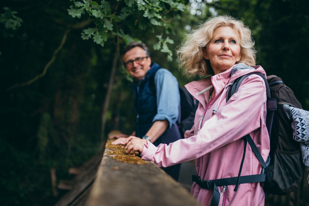 A man and woman stand on a bridge while pausing during a hike.
