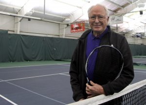 Jim holds a tennis racket on the court of his local tennis club.
