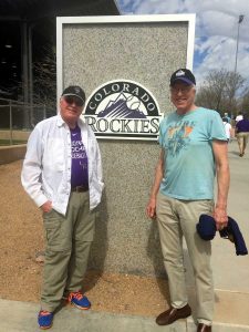 Jim stands next to his brother in front of the Colorado Rockies sign