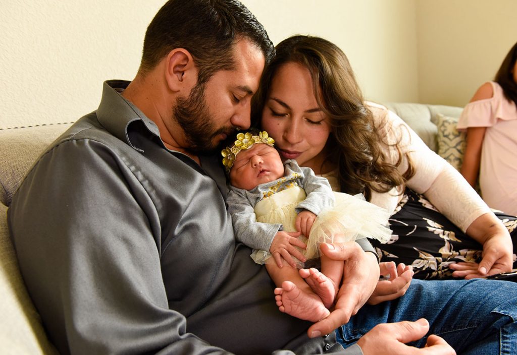 A couple kisses their newborn daughter.