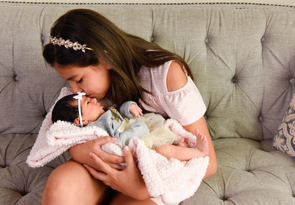 A 10-year-old kisses her  new baby sister.