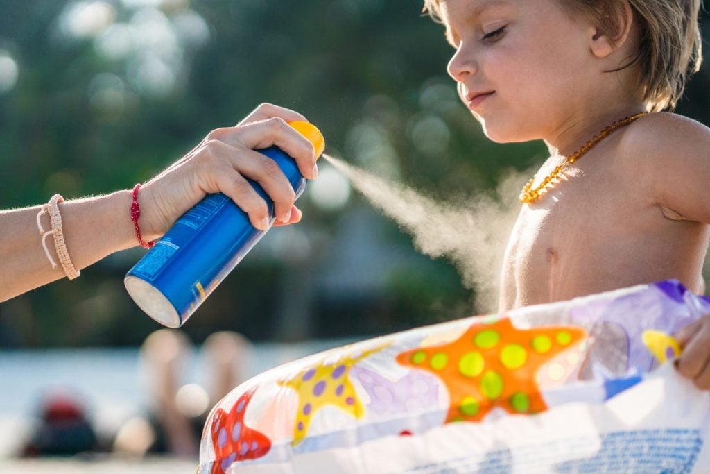 A photo of a child being sprayed with sunscreen.