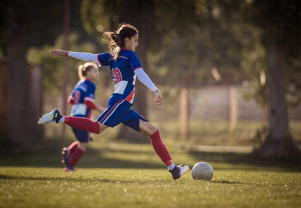 A teenage girl kicks a soccer ball during a game.