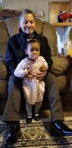 Grandfather smiles while holding his granddaughter between his legs.