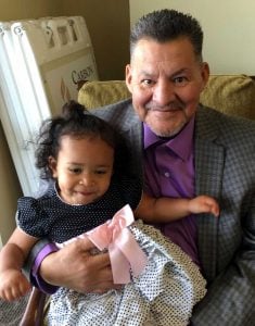 grandfather smiles holding smiling granddaughter on his lap.