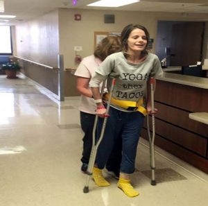 women walking with crutches and nurses help through a hospital hallway.