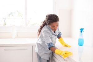 woman disinfecting coronavirus by wiping down countertops in the kitchen, details which are answered in the COVID-19 FAQ.