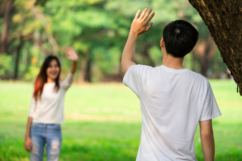 to people stand six feet apart pretending to give each other high five, demonstrating what is social distancing.