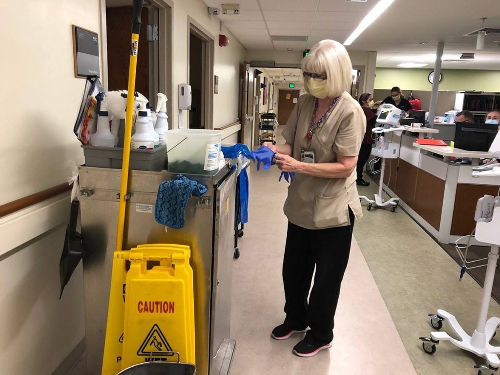 hospital housekeepers, like this one wearing a mask and gloves, are on the front lines during covid pandemic.