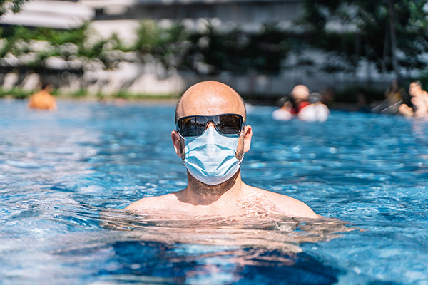  A man in mask and sunglasses at a swimming pool in this article about if it is safe to swim during covid