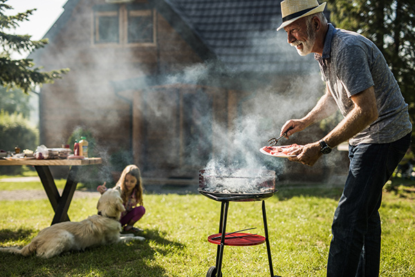 Grilling myths busted. An older man grills with a little girl and a dog in the backround.