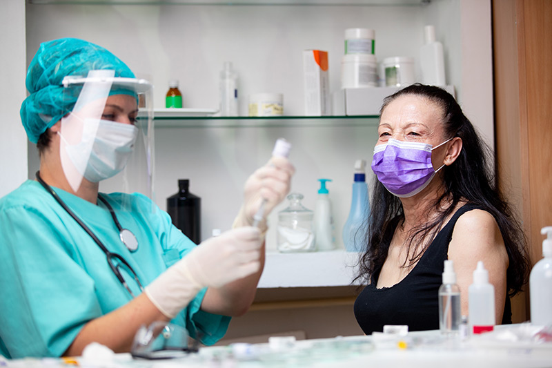 nurse with mask and shield readies a coronavirus vaccine for a patient wearing a mask.