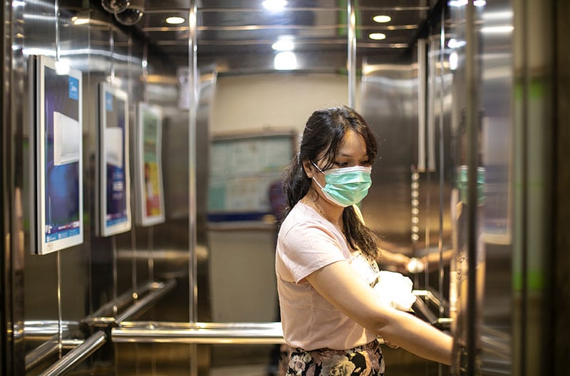 woman wearing mask in an elevator, a place were airborne coronavirus transmission would be more likely to happen.